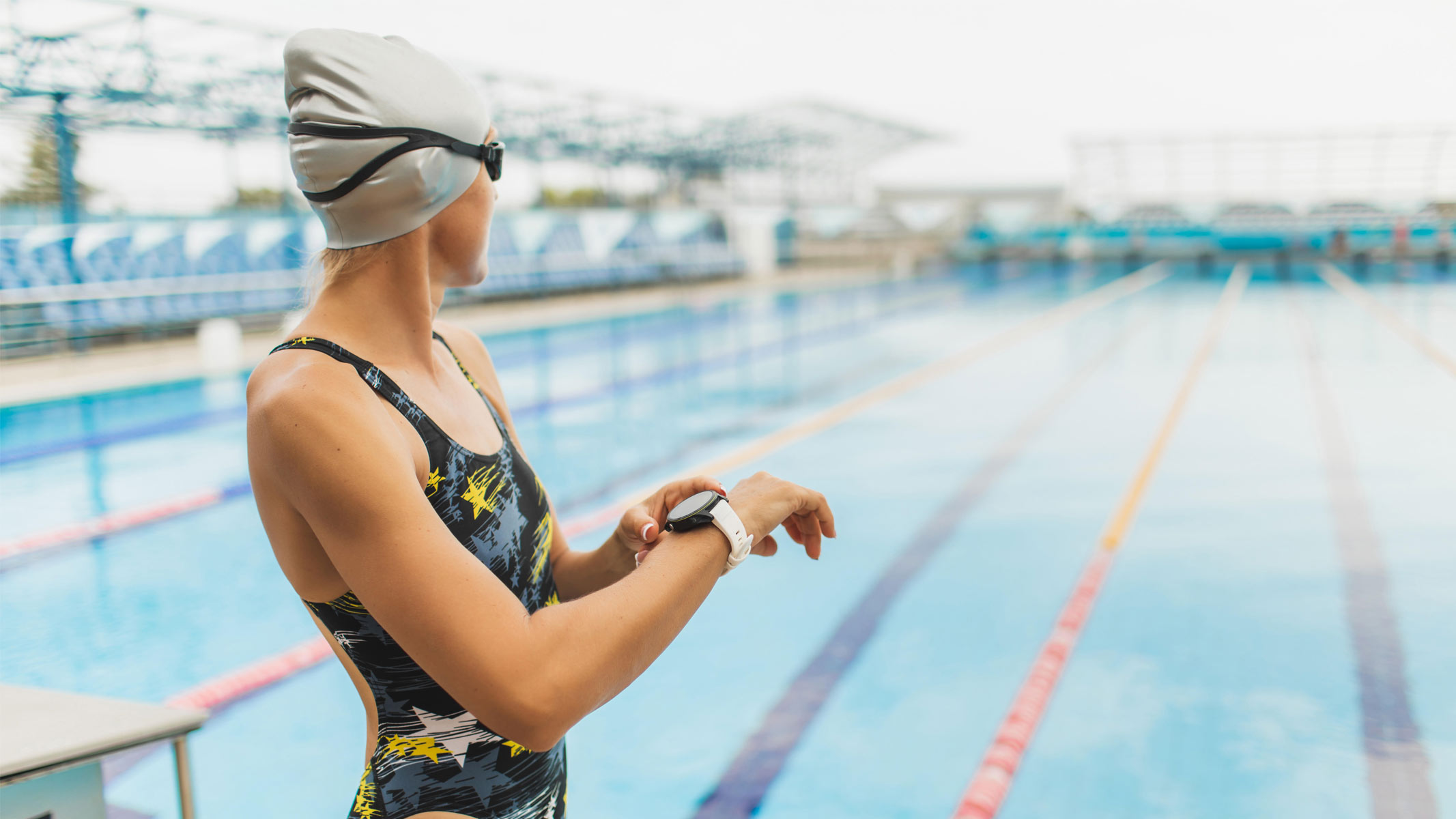 A woman stood by the side of a swimming pool using a fitness tracker.