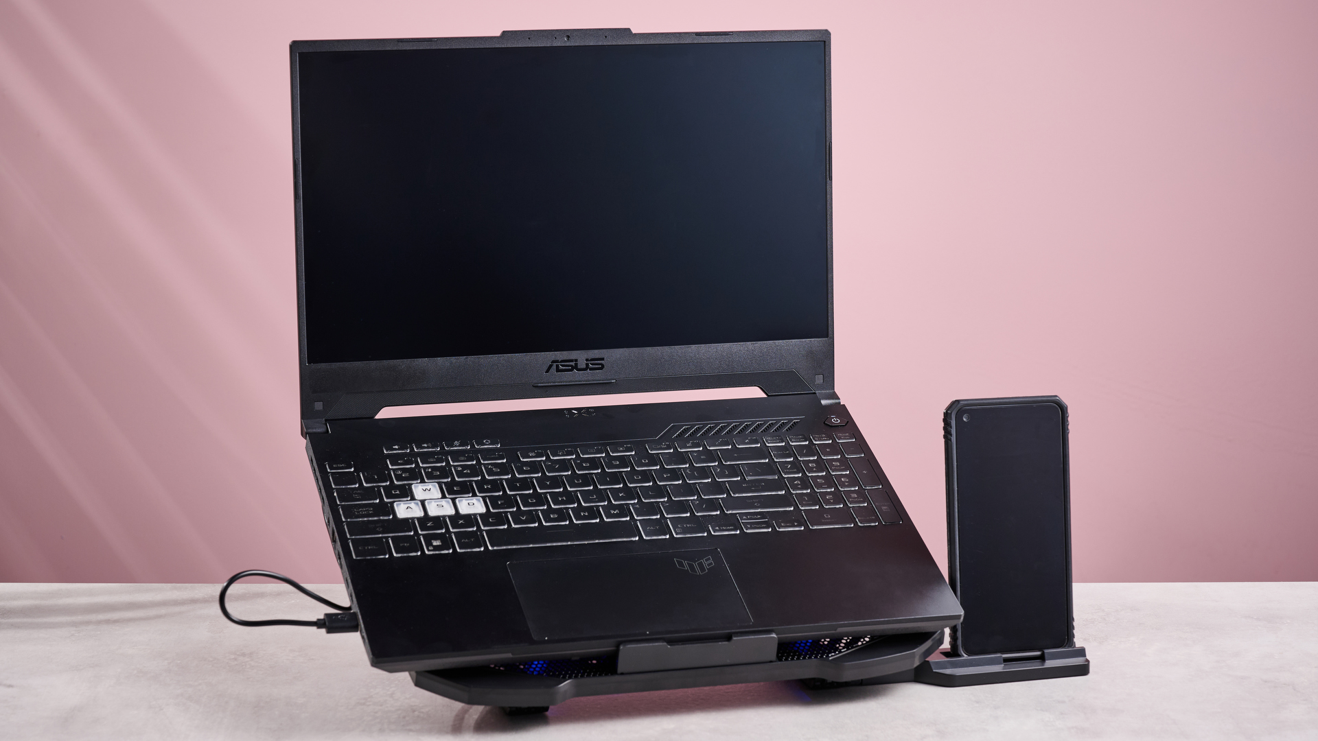 The Aimuzi F2 Plus laptop cooling pad holding up a gaming laptop and a smartphone in front of a pink background.