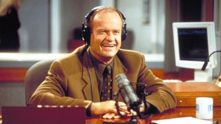 A still of Frasier Crane from the TV show, he's in a recording studio wearing headphones and smiling with a mic in front of him.