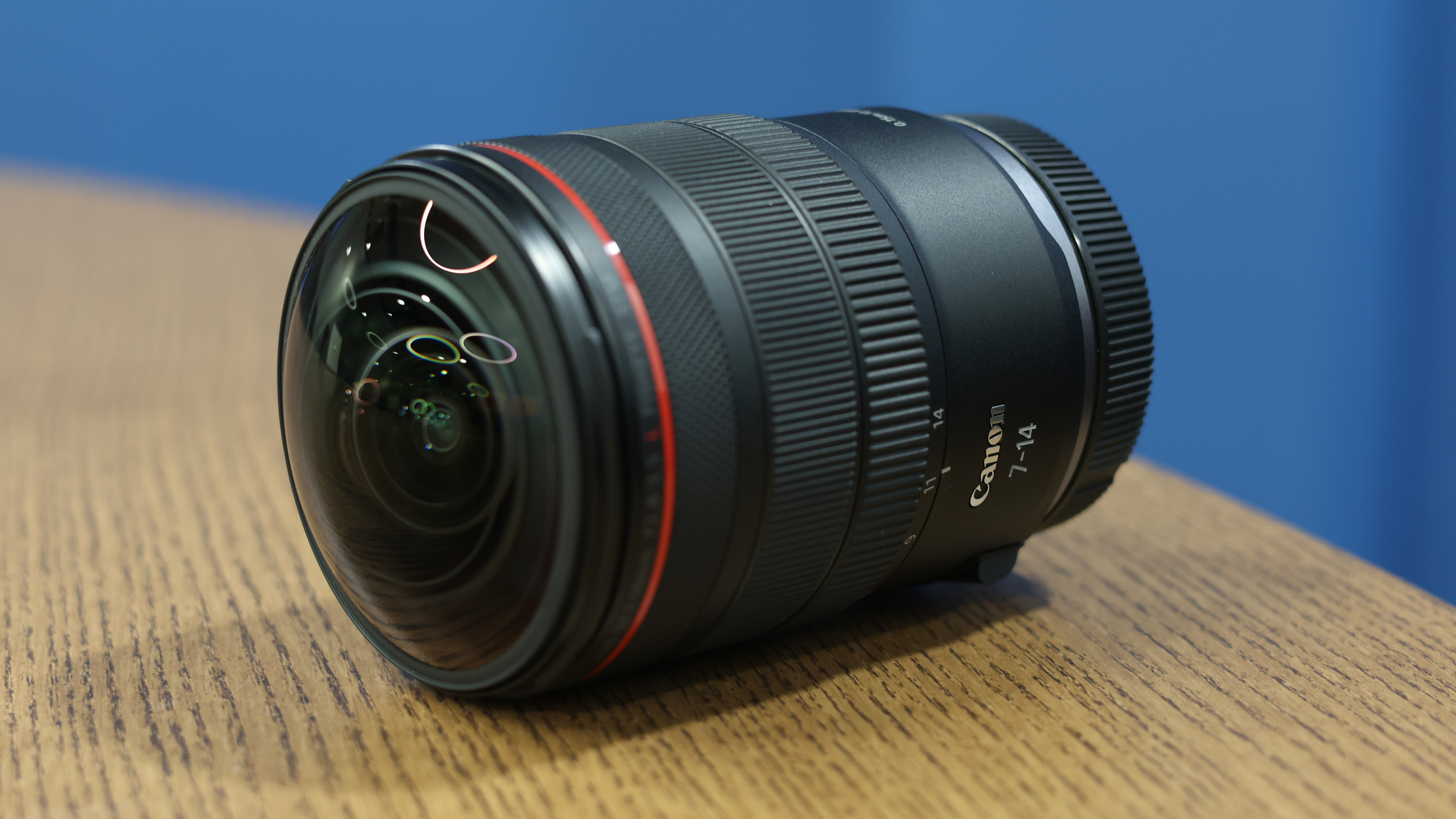 Canon RF 7-14mm f/2.8-3.5L Fisheye STM on a wooden surface, in front of a blue background