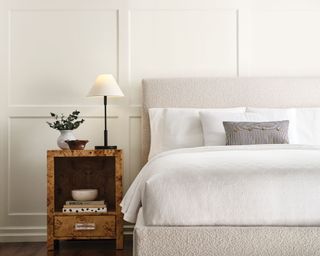 white bedroom with panelled walls, cream boucle bed and brown bedside table with white lamp