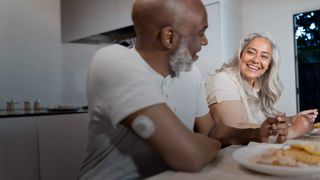 A man and woman sitting at a table with food. The man has a Stelo sensor on his arm.