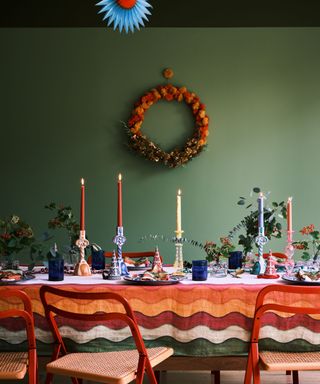 Colorful tablescape with orange tablecloth and candles and wreath