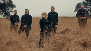 Forlorn stood in a field of tall grass - their singer is wearing a flower crown