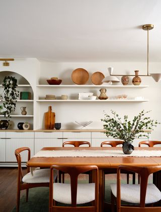 A dining room with white walls, wooden furniture, and open storage on the walls