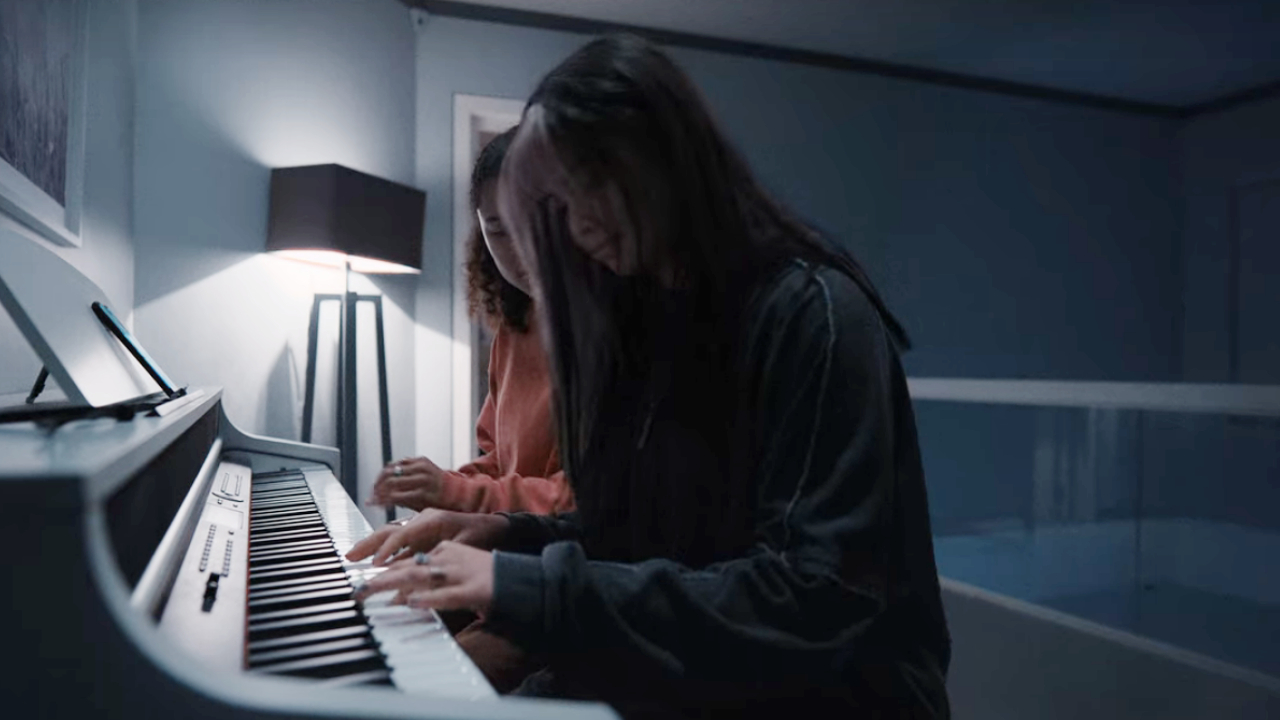 Tamara Smart and Siena Agudong playing the piano together in a bedroom in Resident Evil.