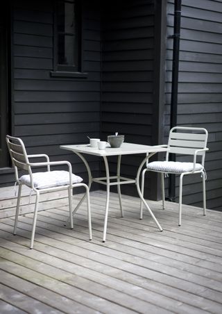 A decked outdoor area with black painted fence in background, and white metal bistro table and chair set