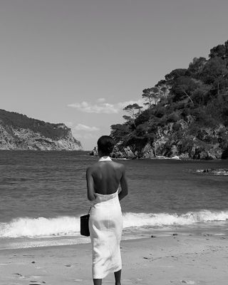 Sylvie Mus wearing a white halter linen dress on the beach.