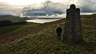 A woman stands near an obelisk overlooking the sea and dark storm clouds at Corrin’s Folly Peel on the Isle of Man in the United Kingdom.