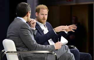 Prince Harry wearing a blue suit sitting in a chair and talking with Andrew Ross Sorkin