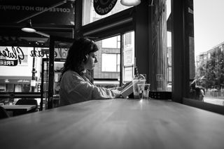 Image of a woman sitting at a cafe reading a book, in black-and-white, taken on the Sigma 18-50mm f/2.8 DC DN | C Canon RF