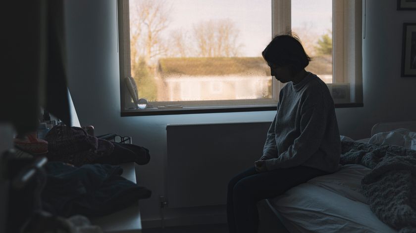 Woman sitting in a dark room with the window blinds open 