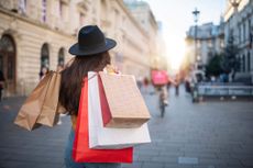 Rear view of woman with a hat walking on the city street and carrying shopping bags.Shopping in sale. Black Friday sale.