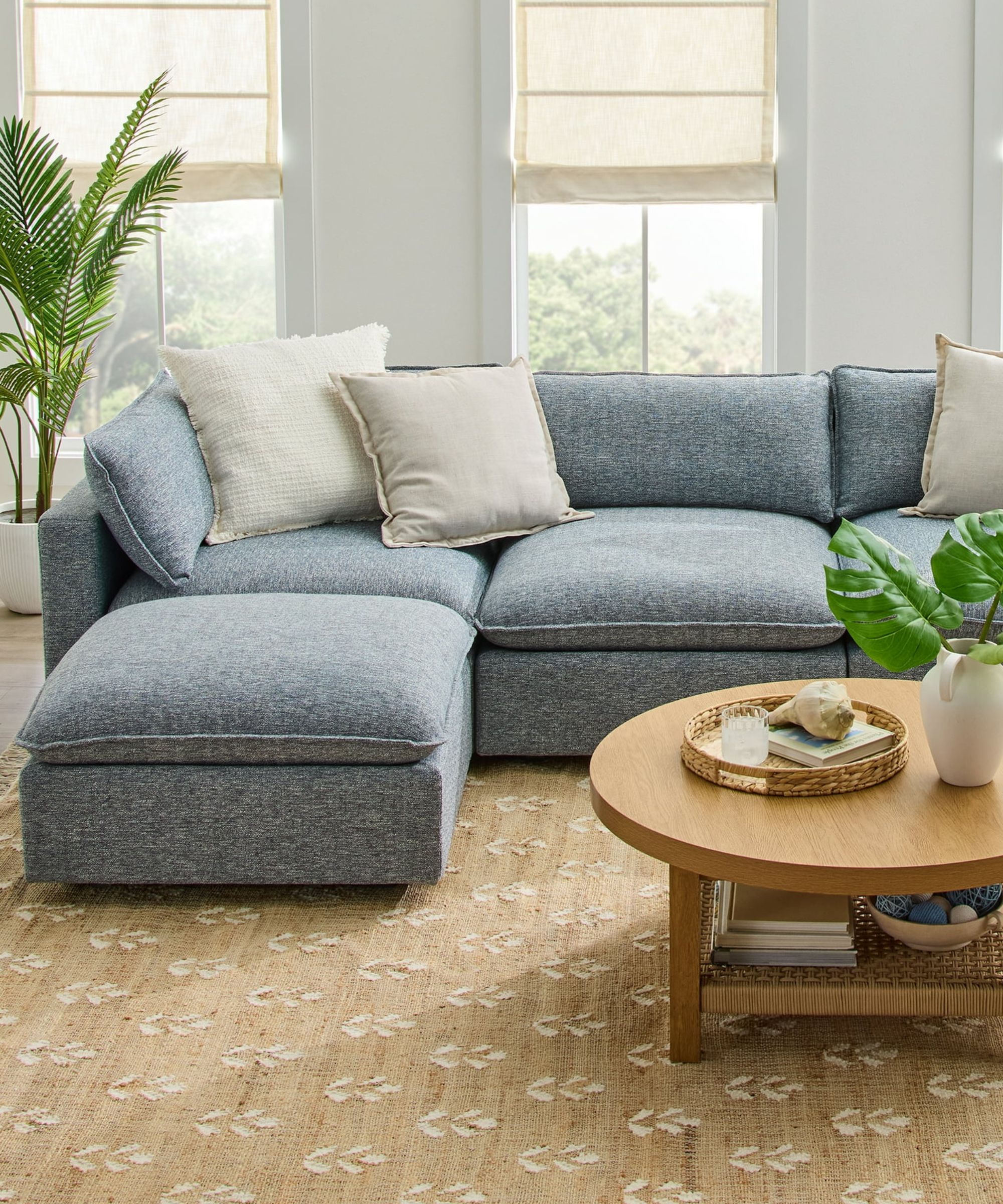 neutral living room with a light blue chaise L shaped couch, rattan flower print rug and wooden round coffee table