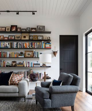 sitting room with gray sofa and chair with bookshelves on white walls