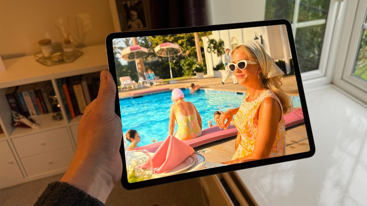 The 13-inch iPad Air being held in one hand. On the screen is an image from Palm Royale.