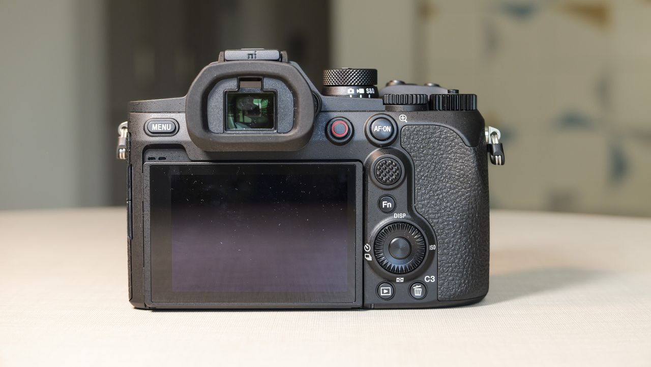 The Sony RX10 V bridge camera on a white table with a patterned wallpaper background, view of its rear, the screen is folded away