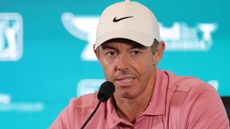 Rory McIlroy wearing a pink polo and white cap speaking in front of a blue sponsor background at his BMW Championship press conference