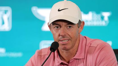 Rory McIlroy wearing a pink polo and white cap speaking in front of a blue sponsor background at his BMW Championship press conference