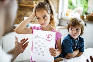 A little girl holding a test paper with a red 'F' on it