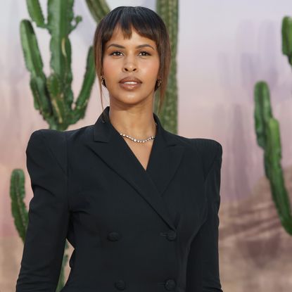 Sabrina Elba wearing a black blazer with shoulder pads and a ponytail hairstyle.