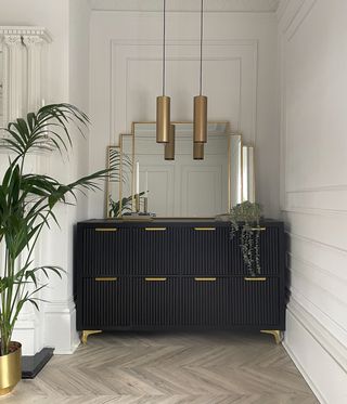 A fluted art deco style credenza in a nook with gold hardware and a gold framed mirror above it