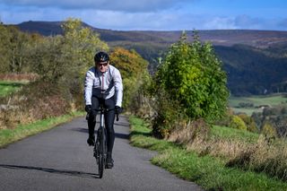 male cyclist riding Ribble Allroad Ti Pro up a hill on a quiet country lane in the Peak District.