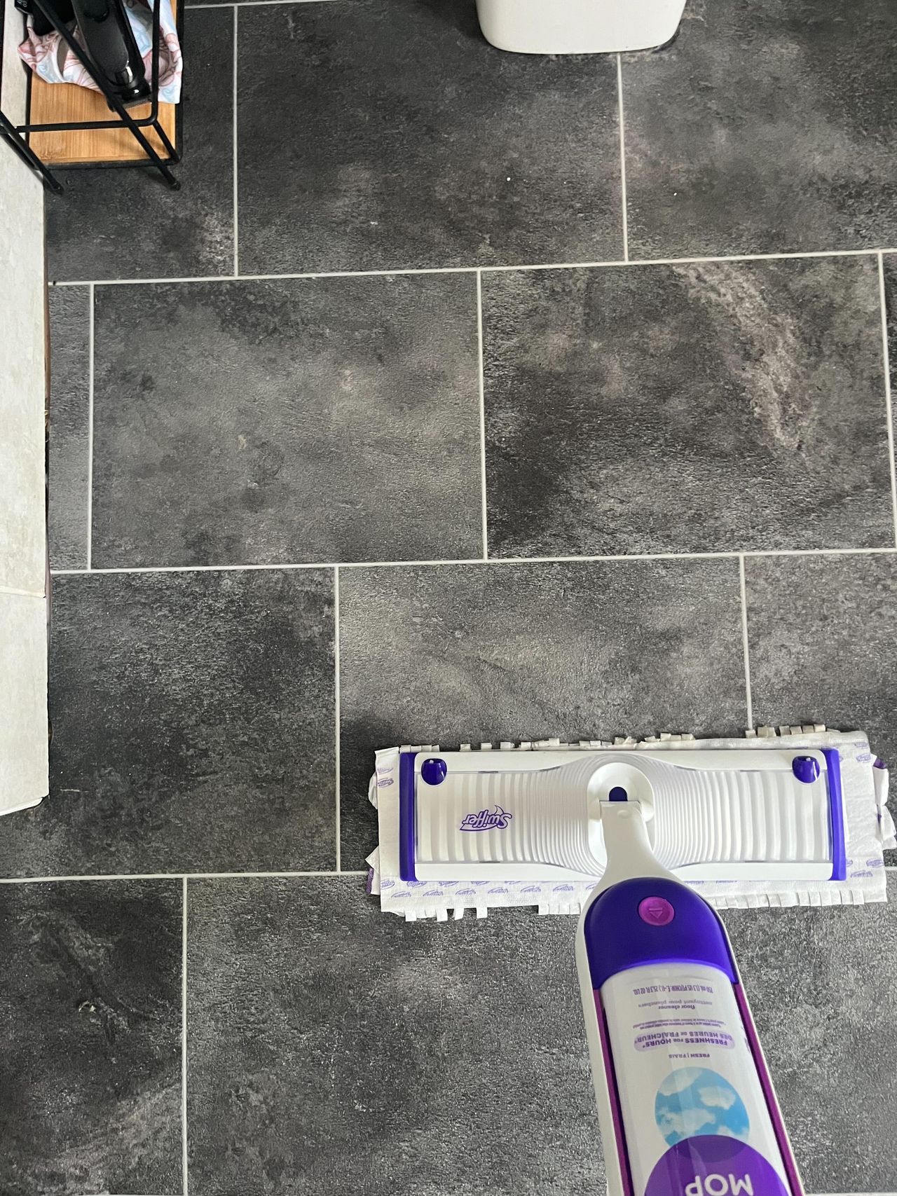 Using a purple and white Swiffer power mop to clean a bathroom floor