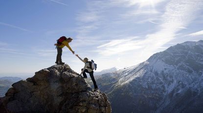 One climber helps another to the top of the mountain