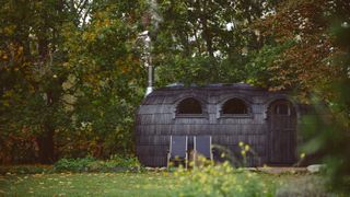 black shingle covered sauna set in garden with seats outside