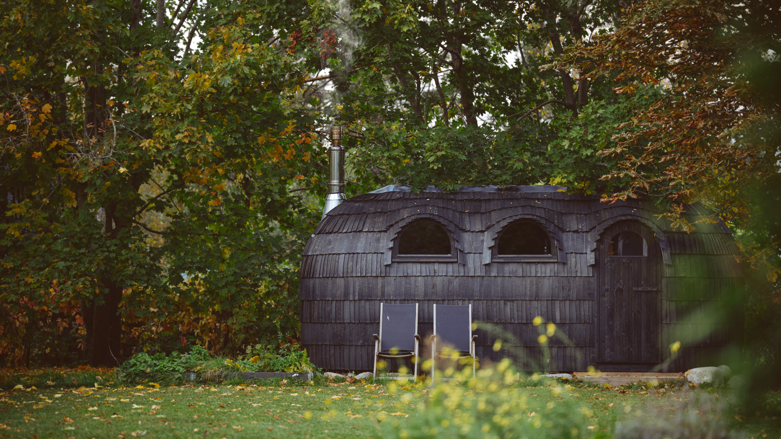 black shingle covered sauna set in garden with seats outside