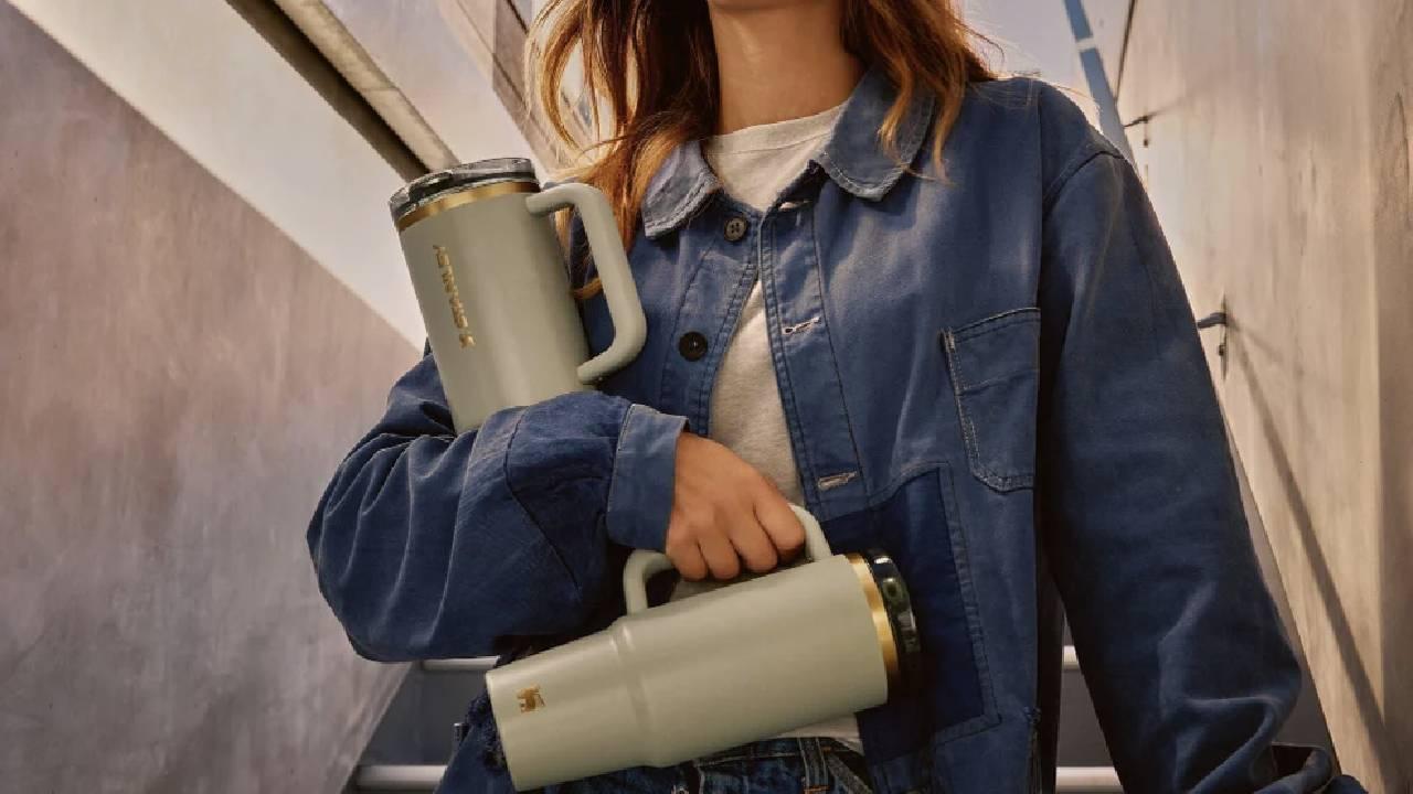 A woman carrying two sage green Stanley Quencher flasks from Stanley.
