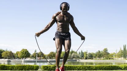 Shirtless muscular man using a jump rope in a park wearing headphones