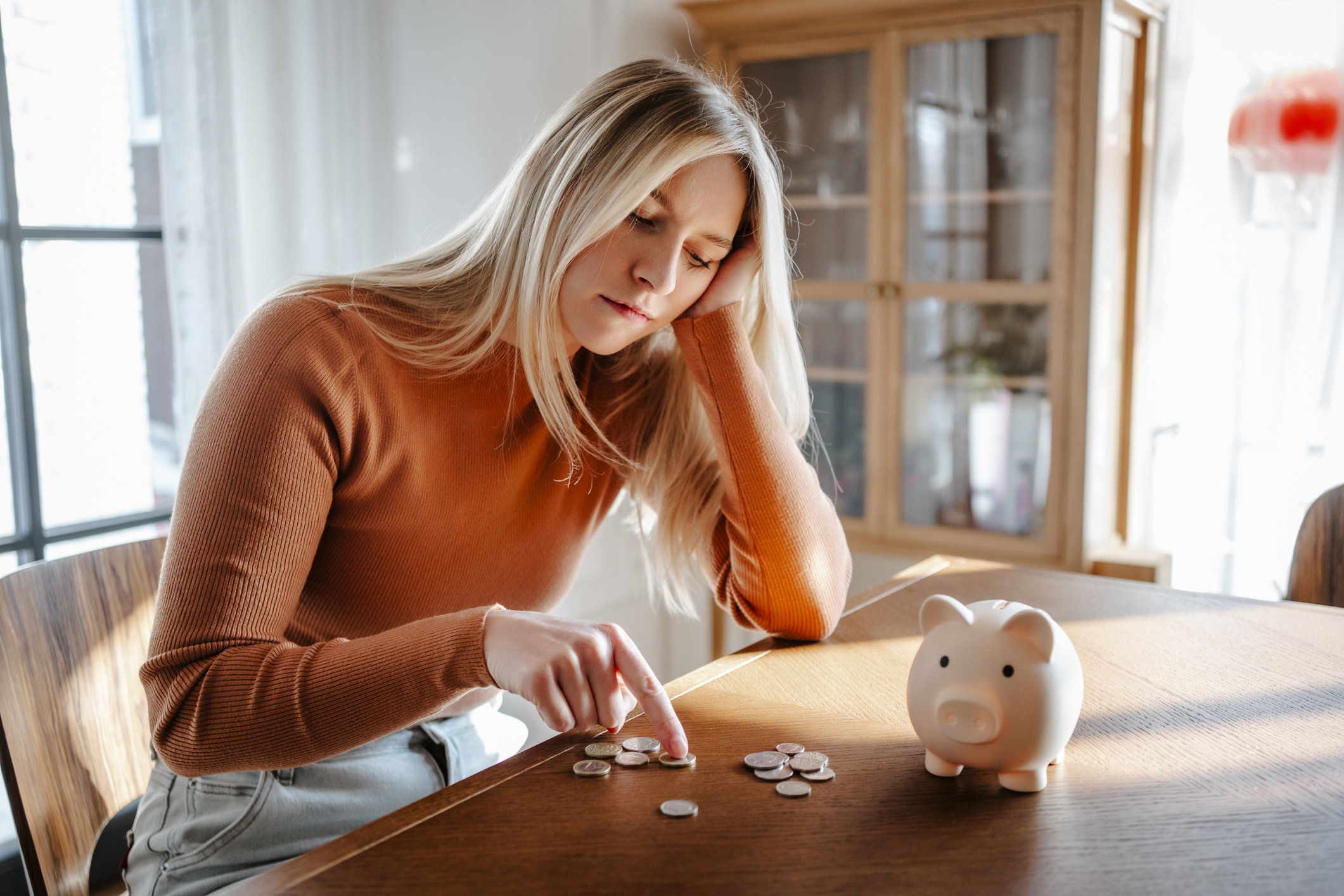 Woman contemplating savings with piggy bank and coins at home