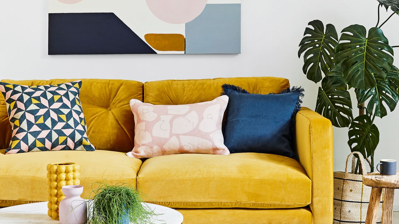 Mustard velvet sofa with colourful cushions beside monstera