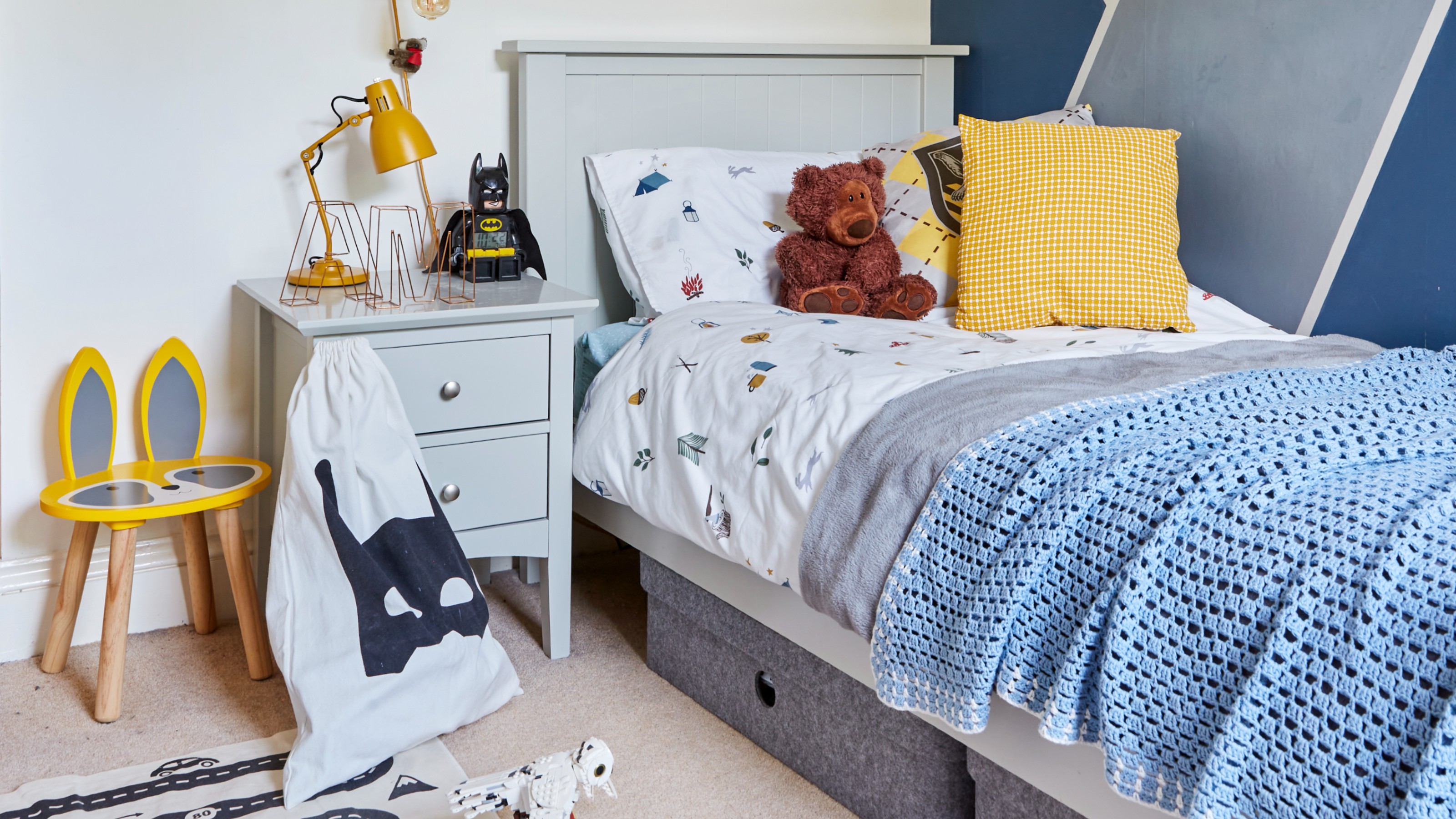 A small boy's bedroom with a single bed with underbed storage and a painted mountain feature wall mural