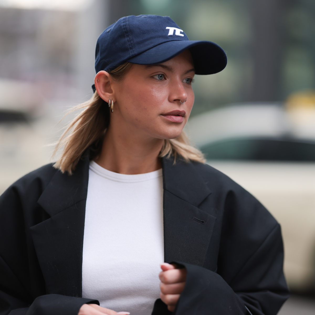 Sophia Geiss seen wearing Thesing navy blue sporty baseball cap, H&M cropped white cotton t-shirt, 032c oversized black relaxed wool coat with wide shoulders, on March 14, 2025 in Berlin, Germany.