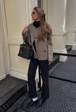 A woman wearing a cropped wool jacket with black trousers and black loafers with white socks.