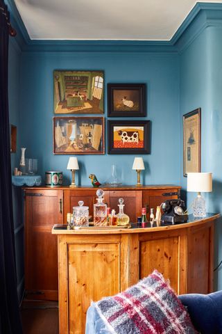 blue living room with wooden bar cart, paintings and wooden sideboard