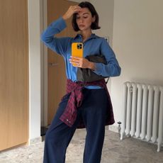 A woman wears a blue sweater, red plaid shirt tied around her waist and navy elevated lounge pants.