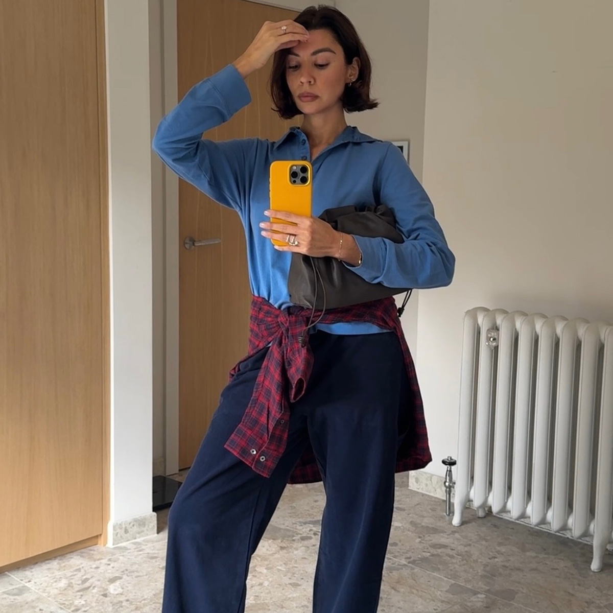 A woman wears a blue sweater, red plaid shirt tied around her waist and navy elevated lounge pants.