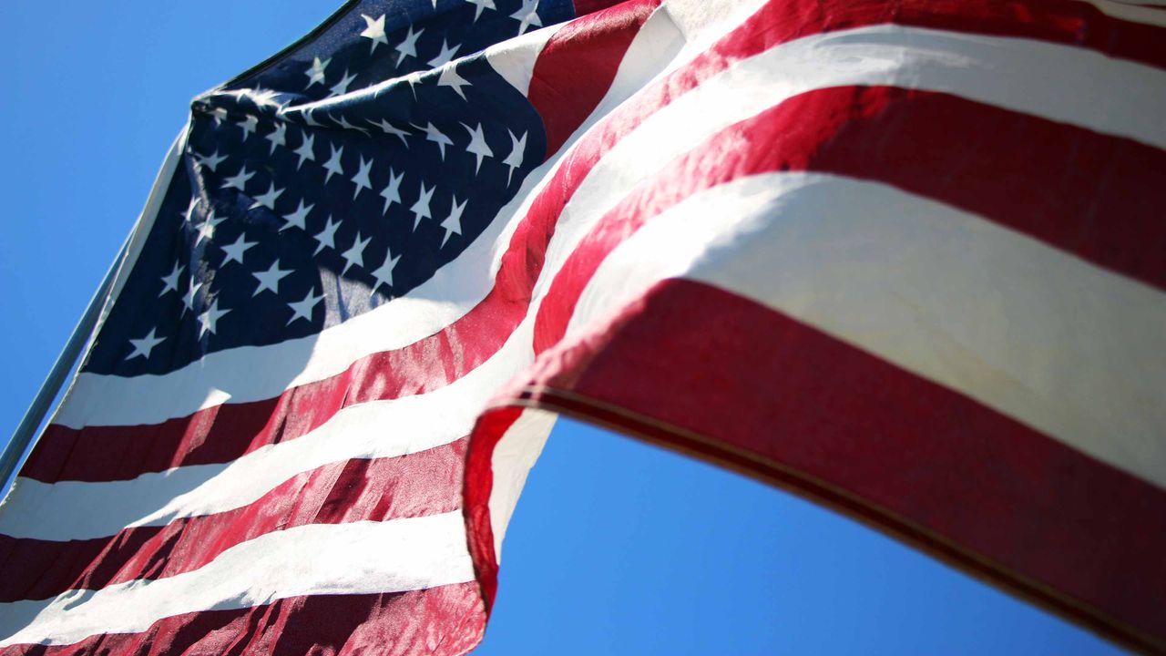 American flag blowing in the wind with blue sky in background