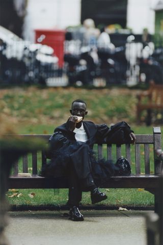 Man wearing Simone Rocha menswear eating sandwich on bench in the park