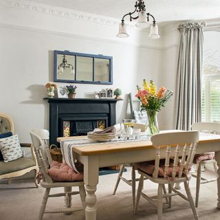 White dining room with fireplace, dining table and spindle chairs, curtains, over mantle mirror