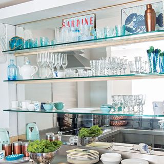 Glass shelves hung over a mirror in a coastal style kitchen