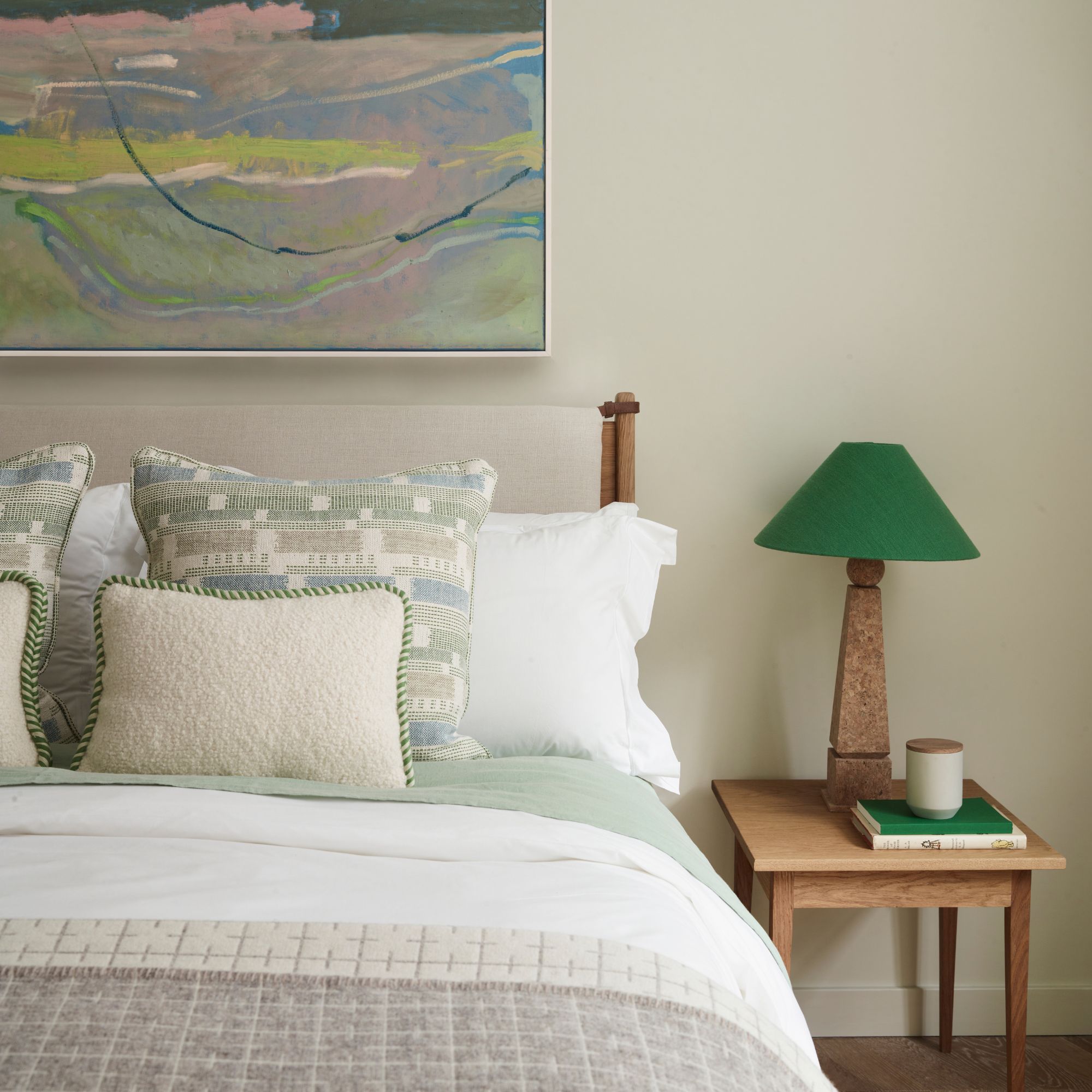 Guest bedroom with wooden accents and neutral bedding, pops of green colour with artwork and lampshade