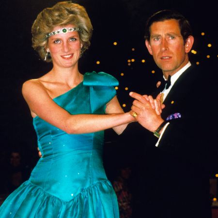 Princess Diana wearing a teal gown with a jeweled headband dancing with Prince Charles in a tuxedo