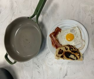 The Always Pan 2.0 beside a plate of bacon, eggs, and pancakes.