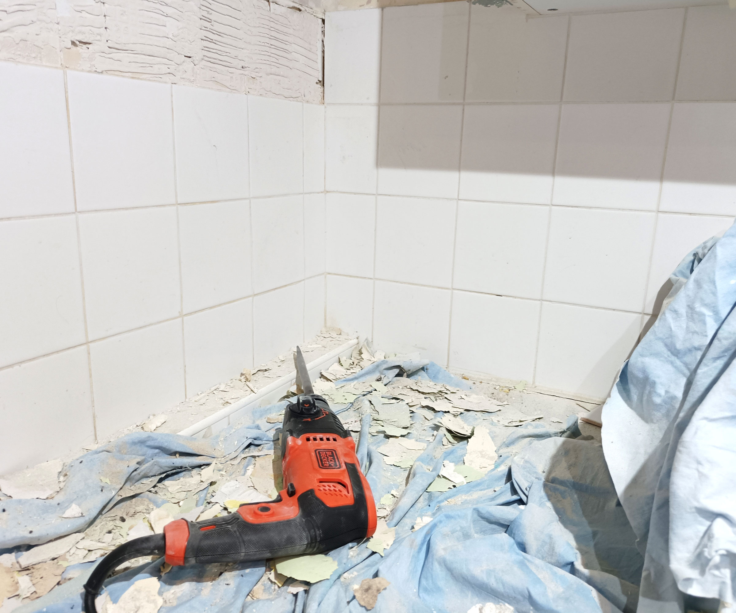 Black and Decker SDS drill lying on a blue dust sheet with debris from the wall and tiles lying around it, with white wall tiles in the background