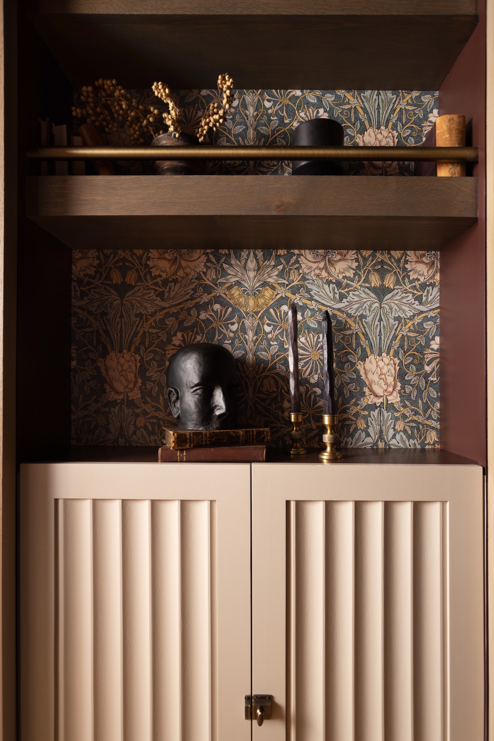 Dark blue, rose and gold floral wallpaper in between shelving with ornaments arranged and fluted cabinetry in beige